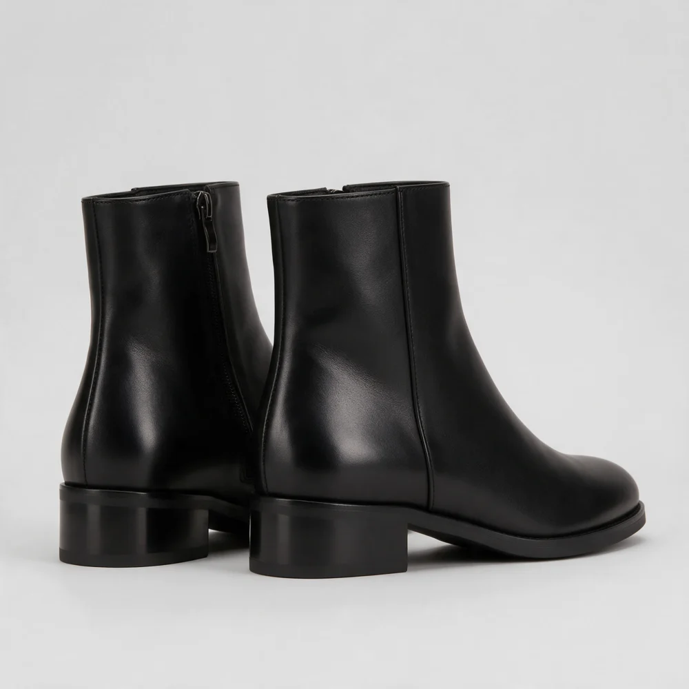 Black leather ankle boots with a low block heel on a light grey background