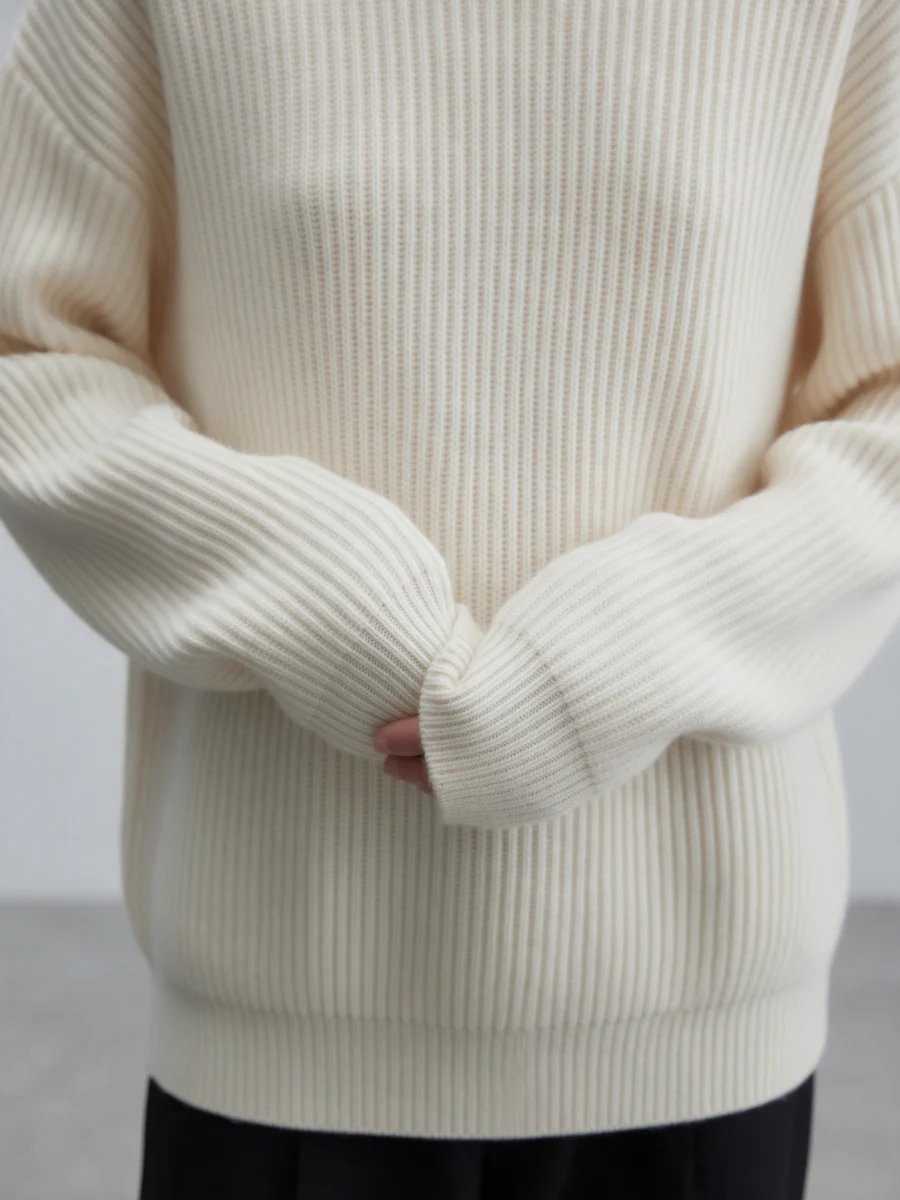 Model wearing a cream ribbed knit sweater with sleeves over the hands