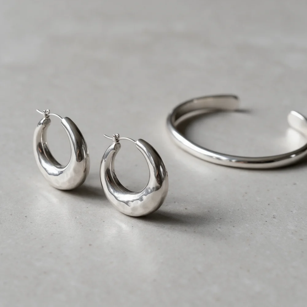 Sculptural silver hoop earrings and a slim cuff on grey stone