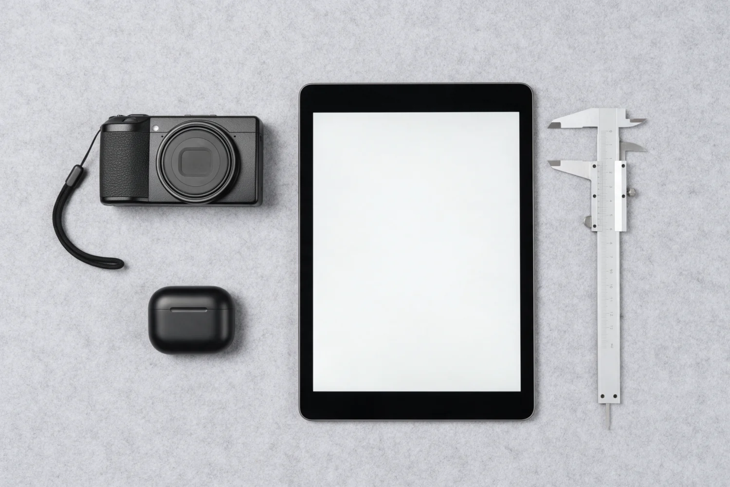 Camera, earbuds case, tablet and caliper laid out for a product review