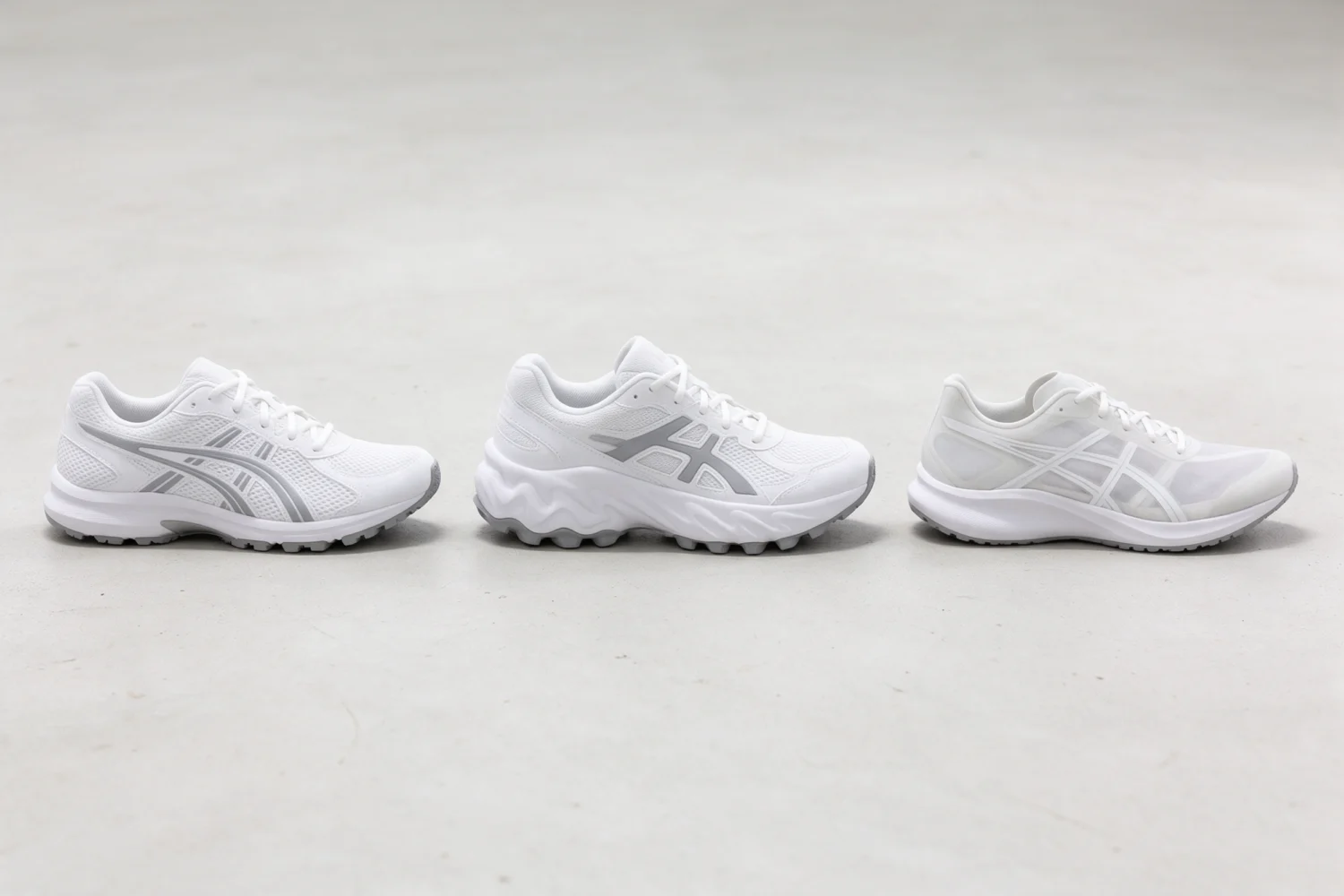 Three pairs of white running shoes lined up on a concrete floor